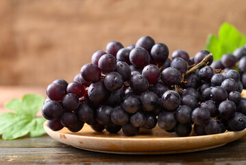 Red grape on wooden plate with black background