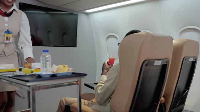 flight attendant is serving refreshments to business class passengers on board the plane.
