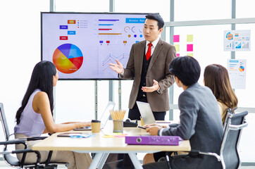 Asian professional successful businessman manager standing showing company growth profit target graph chart presentation on computer monitor to young male and female colleagues in office meeting room