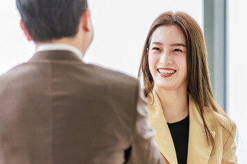 Closeup shot Asian young pretty confident professional successful businesswoman in formal business suit standing smiling shaking hands greeting with unrecognizable businessman in blurred foreground