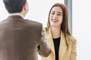 Closeup shot Asian young pretty confident professional successful businesswoman in formal business suit standing smiling shaking hands greeting with unrecognizable businessman in blurred foreground