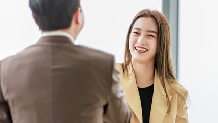 Closeup shot Asian young pretty confident professional successful businesswoman in formal business suit standing smiling shaking hands greeting with unrecognizable businessman in blurred foreground