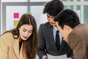 Millennial Asian young professional successful male and female businessman businesswoman worker employee in formal suit standing discussing brainstorming together at working desk in company office