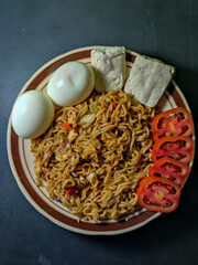 Close up of a plate of instant noodles topped with sliced ​​tomatoes, tofu and boiled eggs isolated on blurred black background