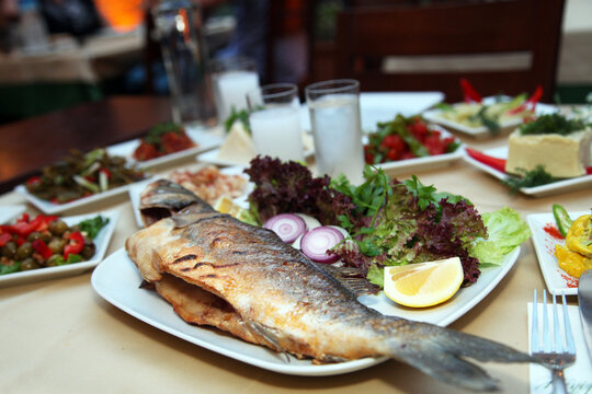 Grilled perch fish (Turkish: Levrek) with appetizer foods and anisette on the restaurant table.