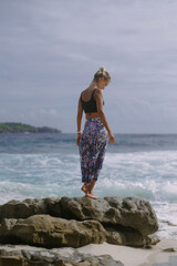 Young woman on a journey. Traveler on a rock by the ocean.