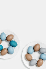 Painted Easter eggs blue, gray, beige colored on round white plate, light background with copy space. Chicken egg pastel shades. Easter holiday food, simple minimal design aesthetic flat lay