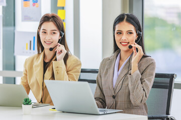 Two millennial Asian young beautiful female customer service call center in formal business suit wearing microphone headset sitting working talking with customers at working desk in company office