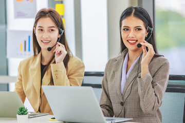 Two millennial Asian young beautiful female customer service call center in formal business suit wearing microphone headset sitting working talking with customers at working desk in company office