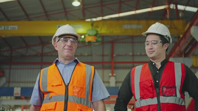 Two engineers high fiving. Caucasian men are 32, 48-year-old wearing safety uniforms and hard hats in a factory. Slow Motion