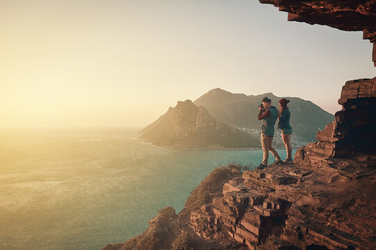 What a great photo opportunity. Full length shot of a young man taking picture of the view while hiking with his girlfriend.