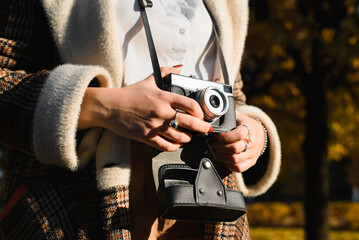 Close-up caucasian female tourist, photographer in coat holding vintage film camera outdoors on sunny day, side view. Concept of travel, tourism, hobby