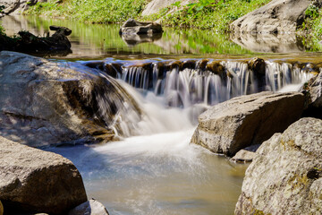Naklejka na ściany i meble Water flowing along rocks in nature, waterfall