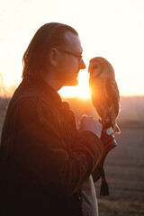 Man and wild bird over sunset sky in field looking on each other Owl symbol of power, wisdom...