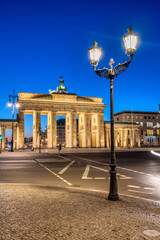 The backside of the illuminated Brandenburg Gate in Berlin with a historic street light at dawn © elxeneize