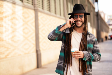 Handsome guy drinking coffee while walking in the street. Modern fashion man using the phone.