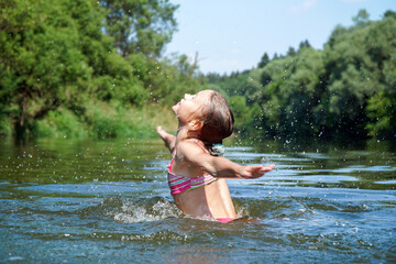Fototapeta premium The girl swims in the river in the summer. Splashes