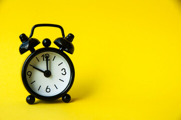 Black alarm clock isolated on yellow background. The clock set at 10 o'clock.