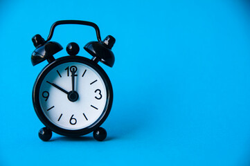 Black alarm clock isolated on blue background. The clock set at 10 o'clock.