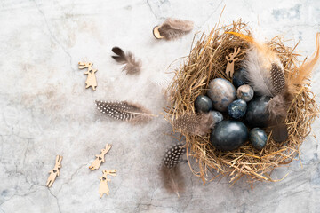 Marble blue Easter eggs in bird nest with feathers and copy space. Happy Easter holiday, top view, flat lay . Horizontal photo. Hibiscus eggs, naturally colored.