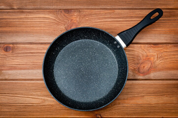 A round frying pan with a plastic handle is a utensil for frying food. Taken against the backdrop of a wooden table surface.