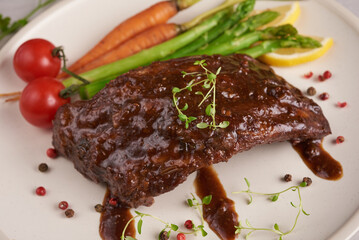 Pork roasted, grilled spare ribs from a summer BBQ served with Vegetables, asparagus, baby carrots, fresh tomatoes and  spices. smoked ribs in white plate on stone background . top view.