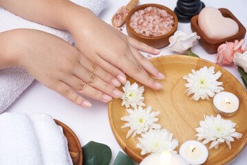 Obraz na płótnie Canvas Woman soaking her hands in bowl of water and flowers, Spa treatment and product for female feet and hand spa, massage pebble, perfumed flowers water and candles, Relaxation. Flat lay. top view.