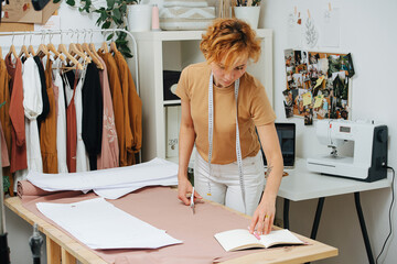 Focused seamstress checking patterns and notes on unrolled fabric on the table.
