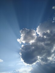 The rays of the sun come out from behind the clouds in the blue sky