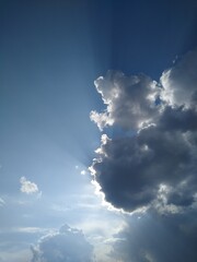 The rays of the sun come out from behind the clouds in the blue sky