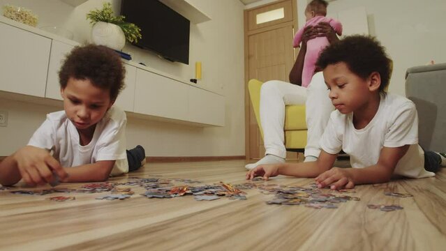 Black family in the room - brothers do a pazzle and only father playing with baby daughter