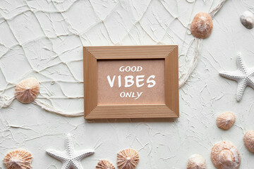 Text Good Vibes only in golden frame. Off white background with starfish, shells, seashells,...