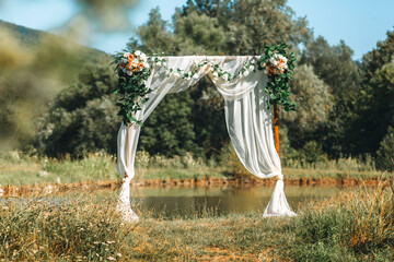 decorated wedding arch on a sunny summer day on the shore of a reservoir against the background of...