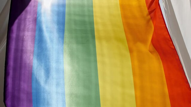 Rainbow LGBT flag in hand and waving on sunset in sunny rays. Lesbian, gay, bisexual, transgender social movements. High quality 4k footage