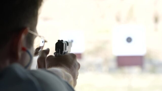 Man shoots with a revolver at targets on the shooting range, close up, blurred focus. Back view of man shooting pistol at target while practicing. Slow motion