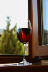 Glass of red wine stands on wooden windowsill