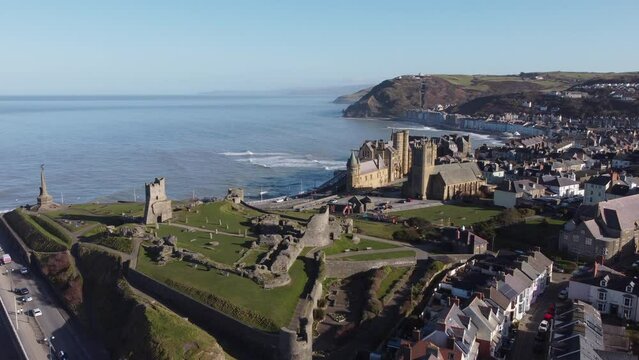An aerial view of the the Welsh town of Aberystwyth showing the castle ruin and seafront. Flying left to right over the town on a sunny spring morning, Ceredigion, Wales, UK.