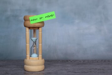 Sandglass and sticky note with text NOW OR NEVER. Copy space for text.