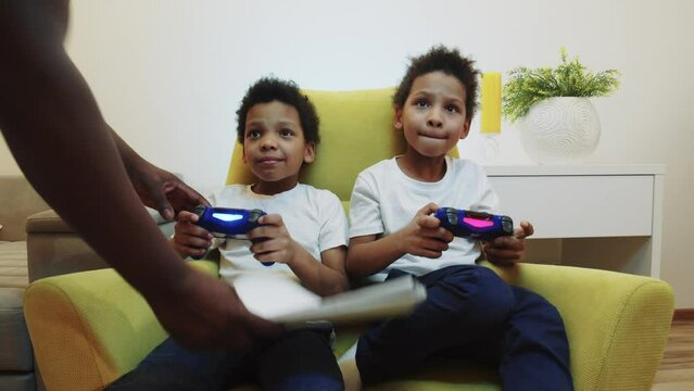 Two little black boys brothers playing game and their parent brings their homework instead of joysticks