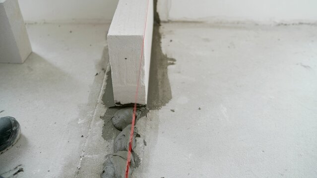 The worker begins the first row of masonry construction in white gas blocks. A worker erects a wall of aerated concrete blocks in an apartment.