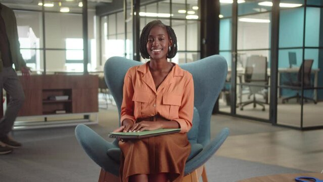 A young african teacher is sitting on the chair in the university, smiling and looking at the camera