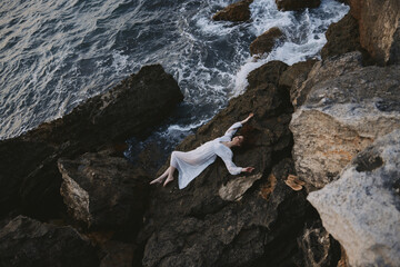 woman in a secluded spot on a wild rocky coast in a white dress Summer vacation concept