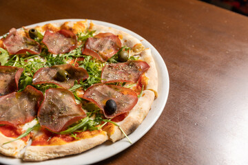 Arugula prosciutto pizza served on white plate