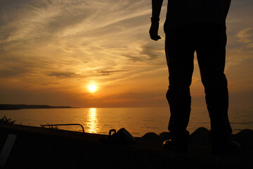 防波堤に立って海に沈む夕日を見ている男性 
