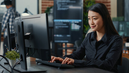 Portrait of smiling asian programer focused on writing code sitting at desk in software development...