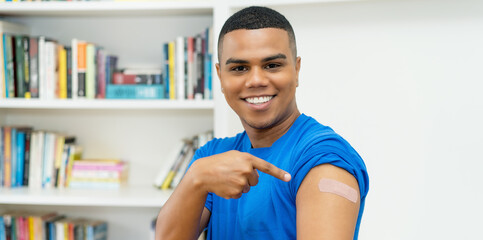 Smiling hispanic young adult man with plaster after vaccination against Covid 19 - obrazy, fototapety, plakaty