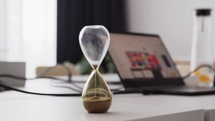 Hourglass sand clock in office, time management for better productivity, closeup shot