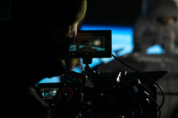 Behind the scenes of commercial shot - Camera operator shooting Caucasian female astronaut stuntwoman hanging on a wires, wearing a spacesuit