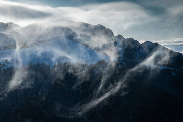 Fototapeta na wymiar Snow blizzard on top of the mountains creating vortex clouds. Freezing winter landscape.