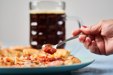 Woman spreading sauce on pizza, beer in background
